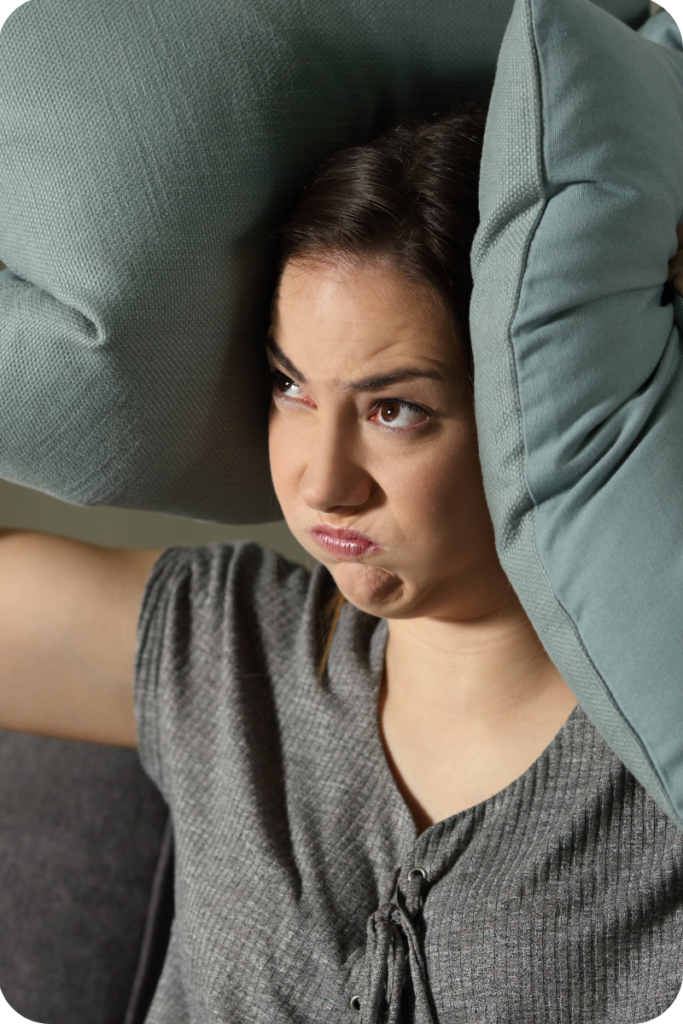 A girl blocking her ears with pillows to prevent noise